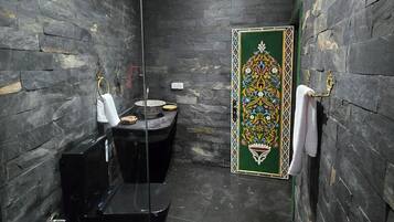 Ein Badezimmer mit dunklen Steinwänden, einer Duschkabine aus Glas, einer Toilette und einer Zierleiste.