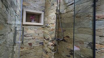 Ducha con puerta de vidrio, pared de piedra y un pequeño estante con un florero.