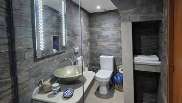 Et moderne badeværelse med stenvæg, glasbrusekabine, vask, toilet og håndklædestang.
