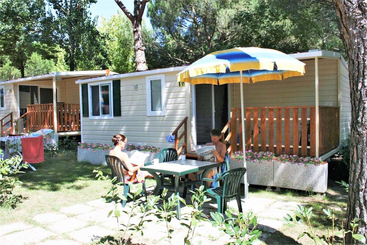 A mobile home with a porch, outdoor seating, and a covered area with an umbrella.