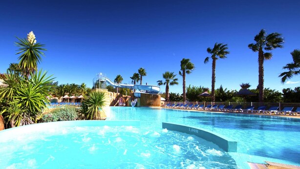 A swimming pool with a water slide, palm trees, and lounge chairs. - Caravan Park Camping L"air Marin, Vias-plage (Vias)