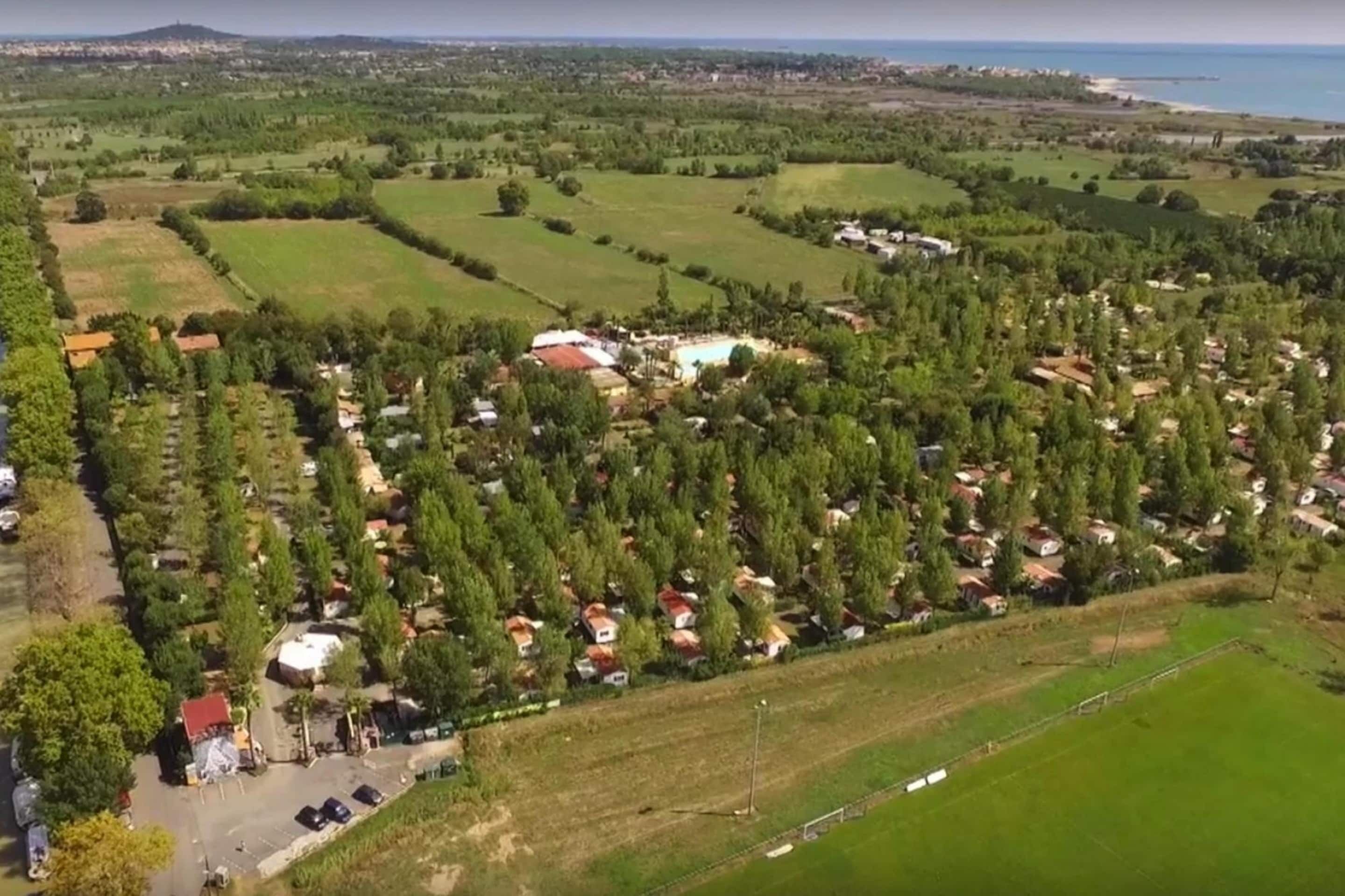 Vista aèria d'una zona residencial amb cases, camps verds i una massa d'aigua a la distància.