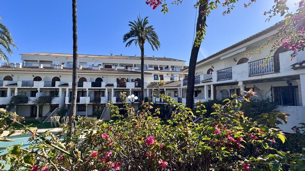 A multi-story hotel with a courtyard, palm trees, and a pool.