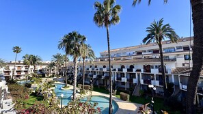 A hotel with multiple floors, a swimming pool, and palm trees.
