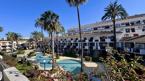 A hotel with multiple floors, a swimming pool, and palm trees.