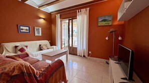 A cozy room with a white sofa, a small table, a TV, and a window with curtains. - Bahia Azul -11   VYBDenia (Denia)