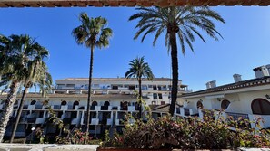 A courtyard with palm trees, a building with multiple balconies, and a clear blue sky.