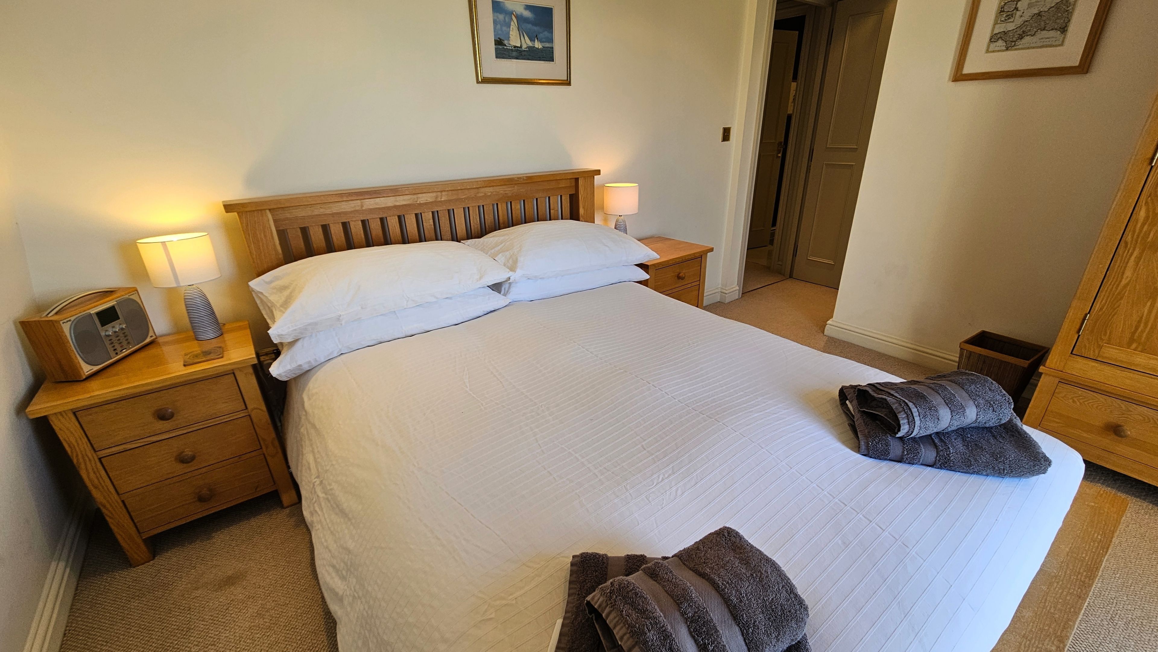 A neatly made bed in a hotel room with a wooden headboard, a bedside table with a lamp, and a radio.