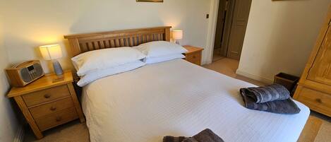 A neatly made bed in a hotel room with a wooden headboard, a bedside table with a lamp, and a radio.
