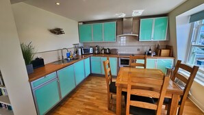 Une cuisine avec des meubles de couleur turquoise, une table à manger en bois et une vue sur la ville par la fenêtre.