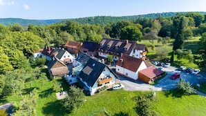 A cluster of traditional houses with sloped roofs, surrounded by lush greenery and a parking area with several cars.