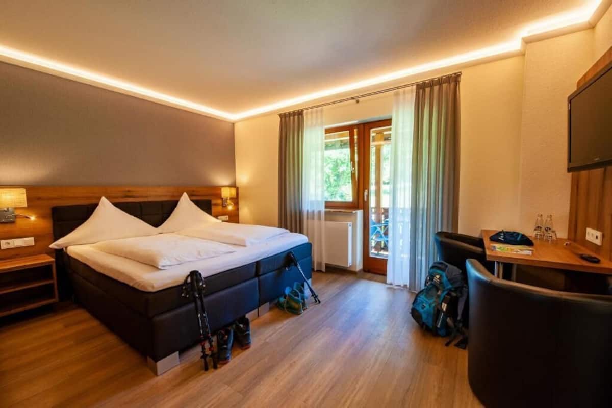A hotel room with a bed, bedside tables, a desk, a chair, and a TV.