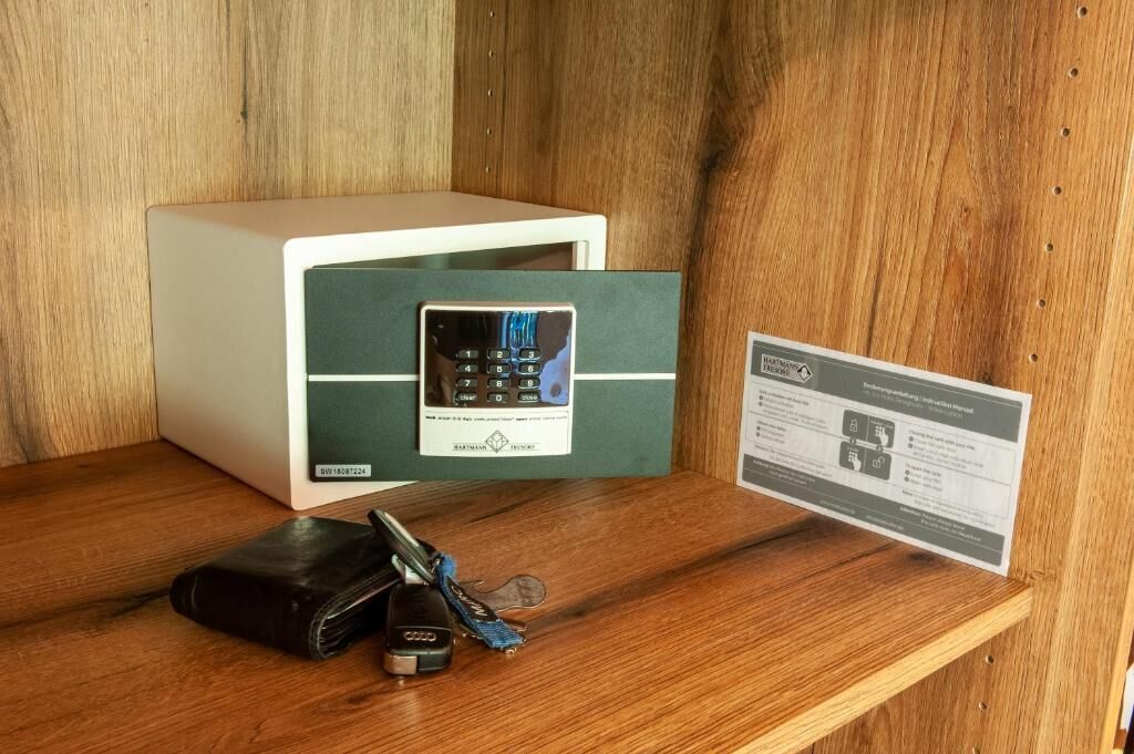 A safe with a keypad, a wallet, keys, and a user manual on a wooden shelf.
