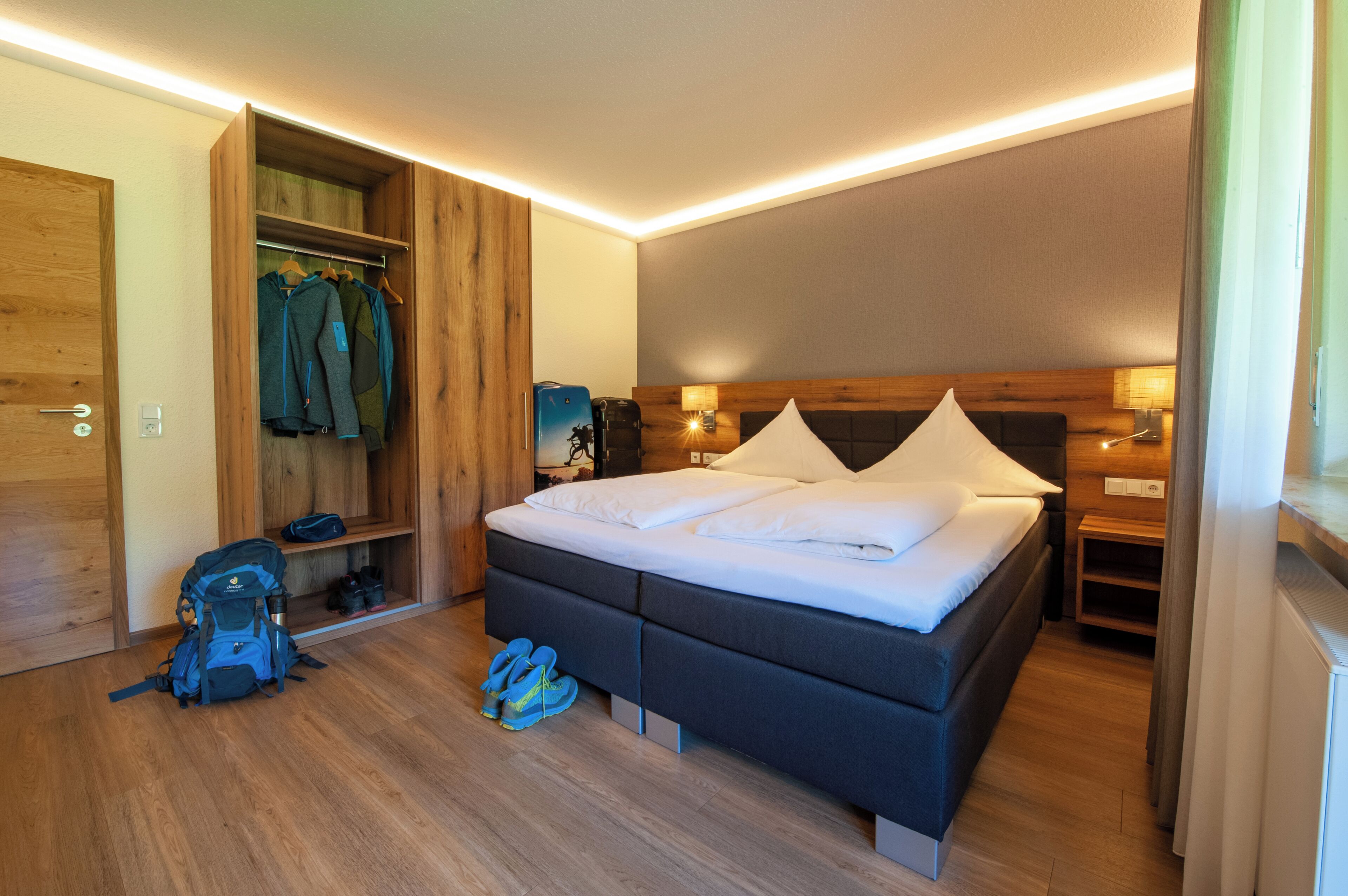 A modern hotel room with a large bed, wooden wardrobe, and a small seating area.