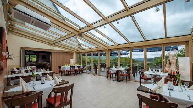 A restaurant with a glass ceiling, tables set with white tablecloths, and a view of the outdoors.