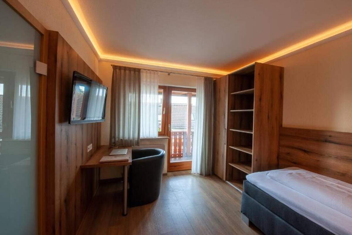 A compact hotel room with a bed, a desk, a chair, and a TV.