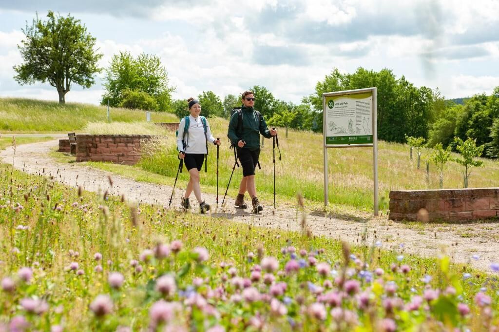 Deux personnes font de la randonnée sur un sentier de terre, avec un panneau indicateur en arrière-plan.