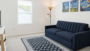 A living room with a dark blue sofa, a patterned rug, a floor lamp, and three paintings on the wall.