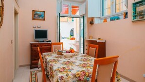 A small dining area with a table set for two, a television on a cabinet, and a window with curtains. - rita's house (Atrani)