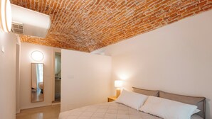 A bedroom with a brick ceiling, a bed with a quilted cover, a bedside lamp, and a mirror on the wall.