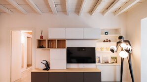 A modern living room with a flat-screen TV mounted on a white cabinet, a wooden coffee table, and a black floor lamp.