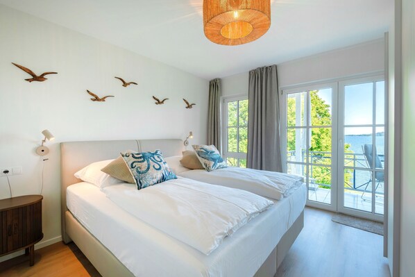 Ein Schlafzimmer mit zwei Betten, einem großen Fenster mit Aussicht, einem Holznachttisch und Vogelzierde an der Wand.