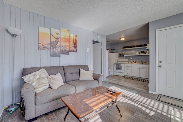 Ein Wohnzimmer mit grauem Sofa, einem Couchtisch und Wandbildern mit Darstellungen von Hirschen.