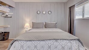 Un dormitorio con cama, mesita de noche, lámpara y espejo en la pared.