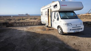 A white RV parked on a dirt surface with a beach and ocean in the background.