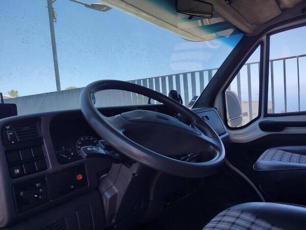 Interior de um veículo com volante, painel e bancos.