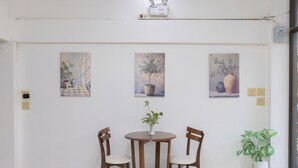 A dining area with a round table and four wooden chairs, flanked by three paintings on the wall, and a potted plant to the side. - Sabai Stay (Hua Hin)