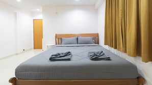 A neatly made bed with a grey bedspread and pillows, a wooden headboard, and a window with brown curtains. - Sabai Stay (Hua Hin)