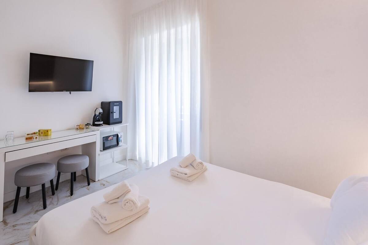 A hotel room with a bed, a desk with a computer, a TV, and a window with curtains.