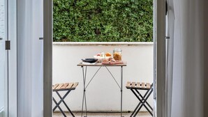 An outdoor patio with a table set for a meal, two wooden chairs, and a view of a green hedge. - Vatican LeM affittacamere (Rome)