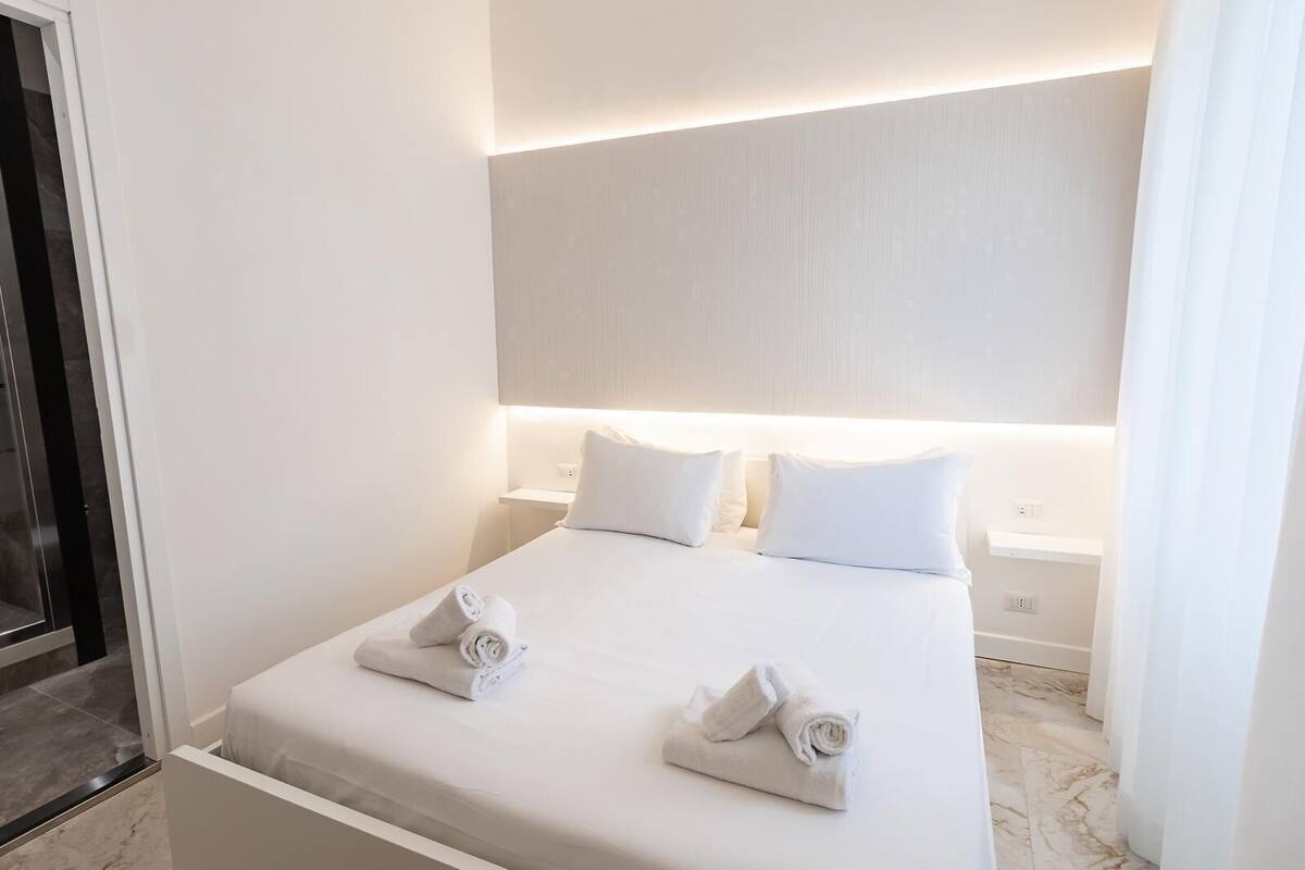 A modern hotel room with a neatly made bed, two pillows, and two rolled towels on the bed.