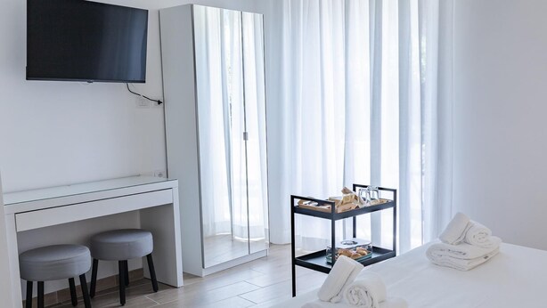A hotel room with a bed, a desk with two chairs, a TV mounted on the wall, a breakfast trolley, and sheer curtains. - Vatican LeM affittacamere (Rome)