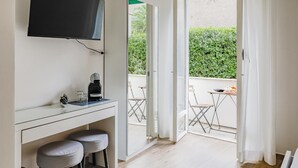 A modern room with a desk, two grey stools, a coffee maker, and a TV mounted on the wall. - Vatican LeM affittacamere (Rome)