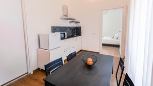 A compact kitchen with white cabinets, a black countertop, and a white refrigerator. There is a dining table with chairs and a decorative bowl on it. - Vatican LeM affittacamere (Rome)