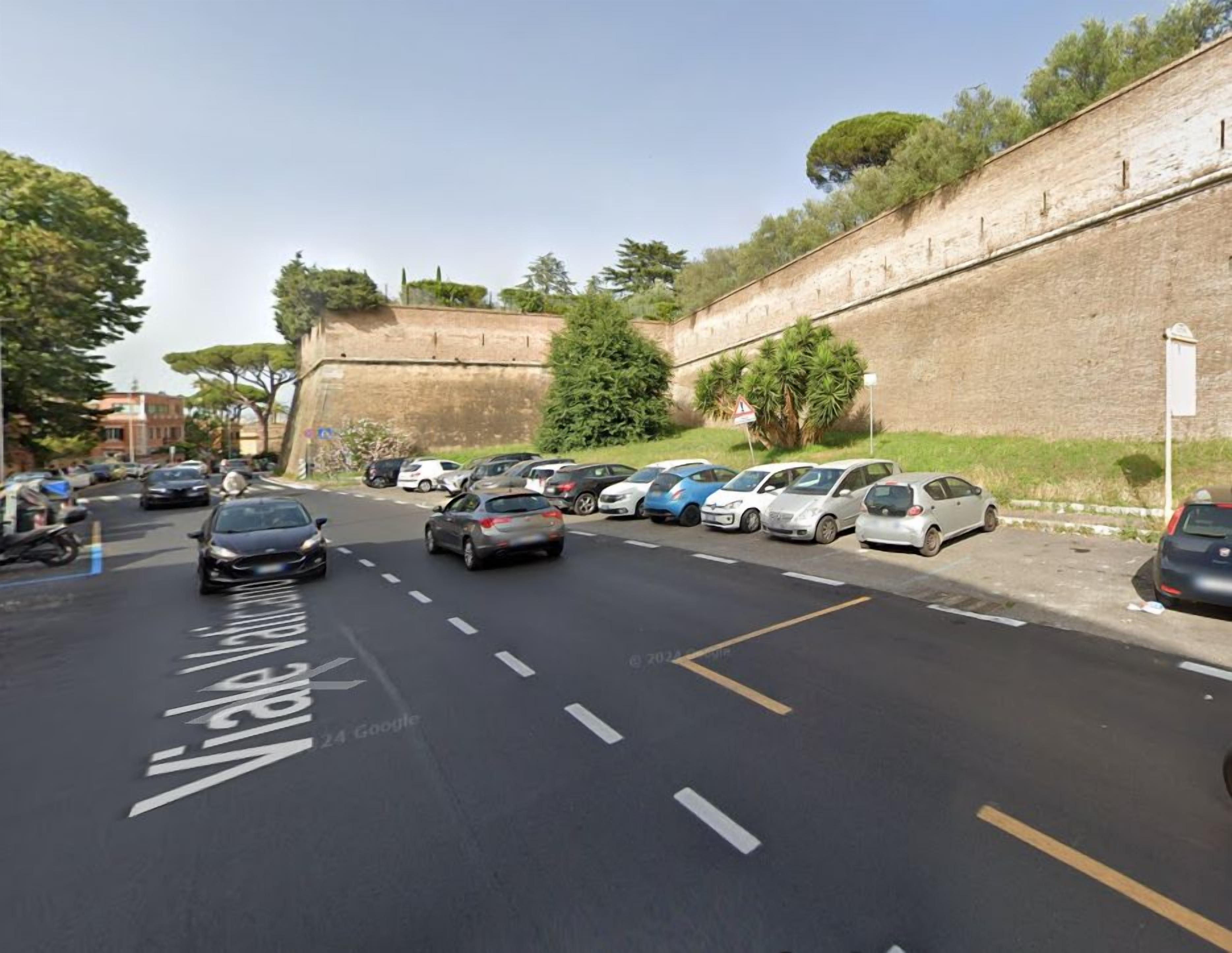 Una calle con autos estacionados y un muro de ladrillo a un lado.