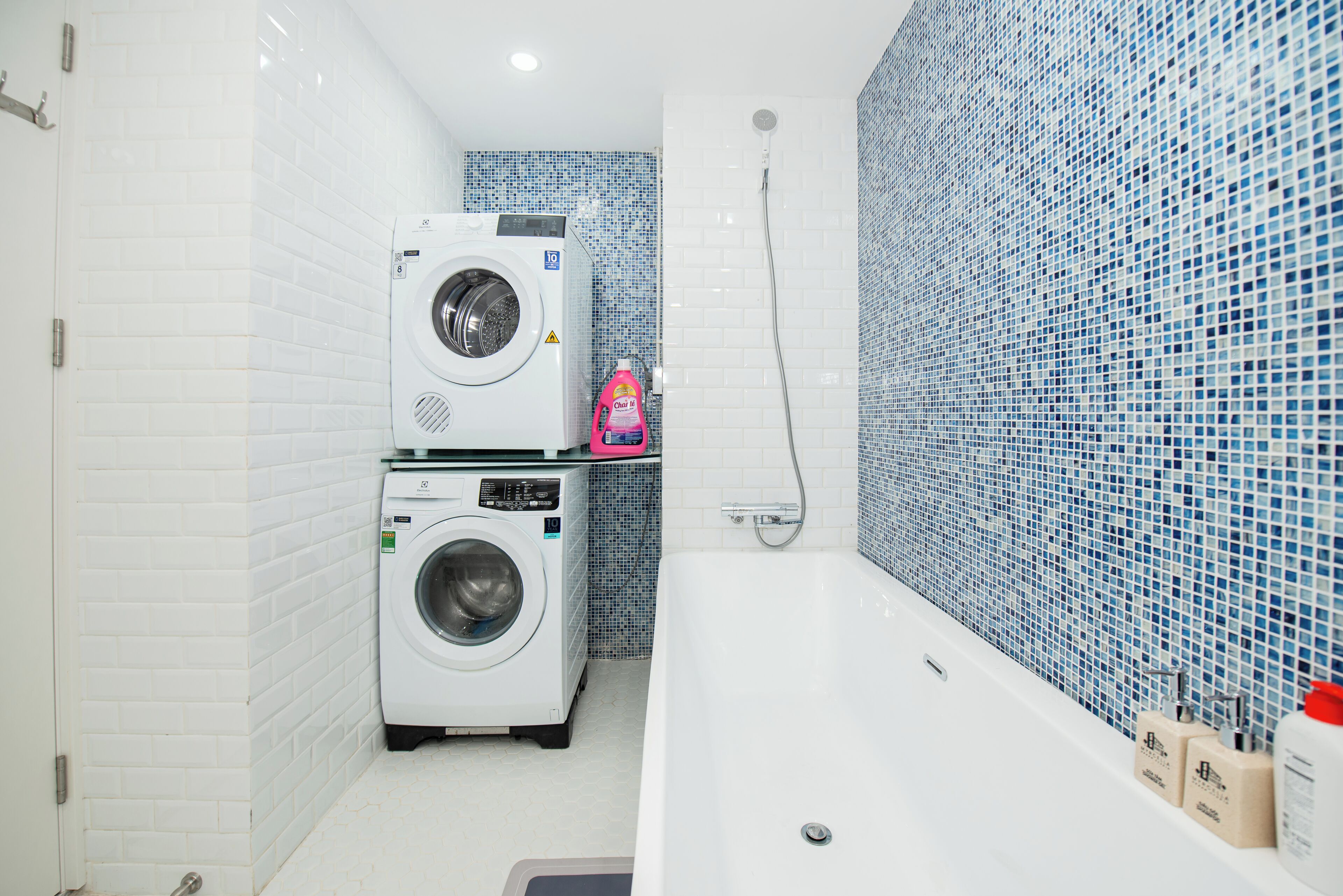 A compact bathroom with a washing machine, a shower, and a tiled wall.