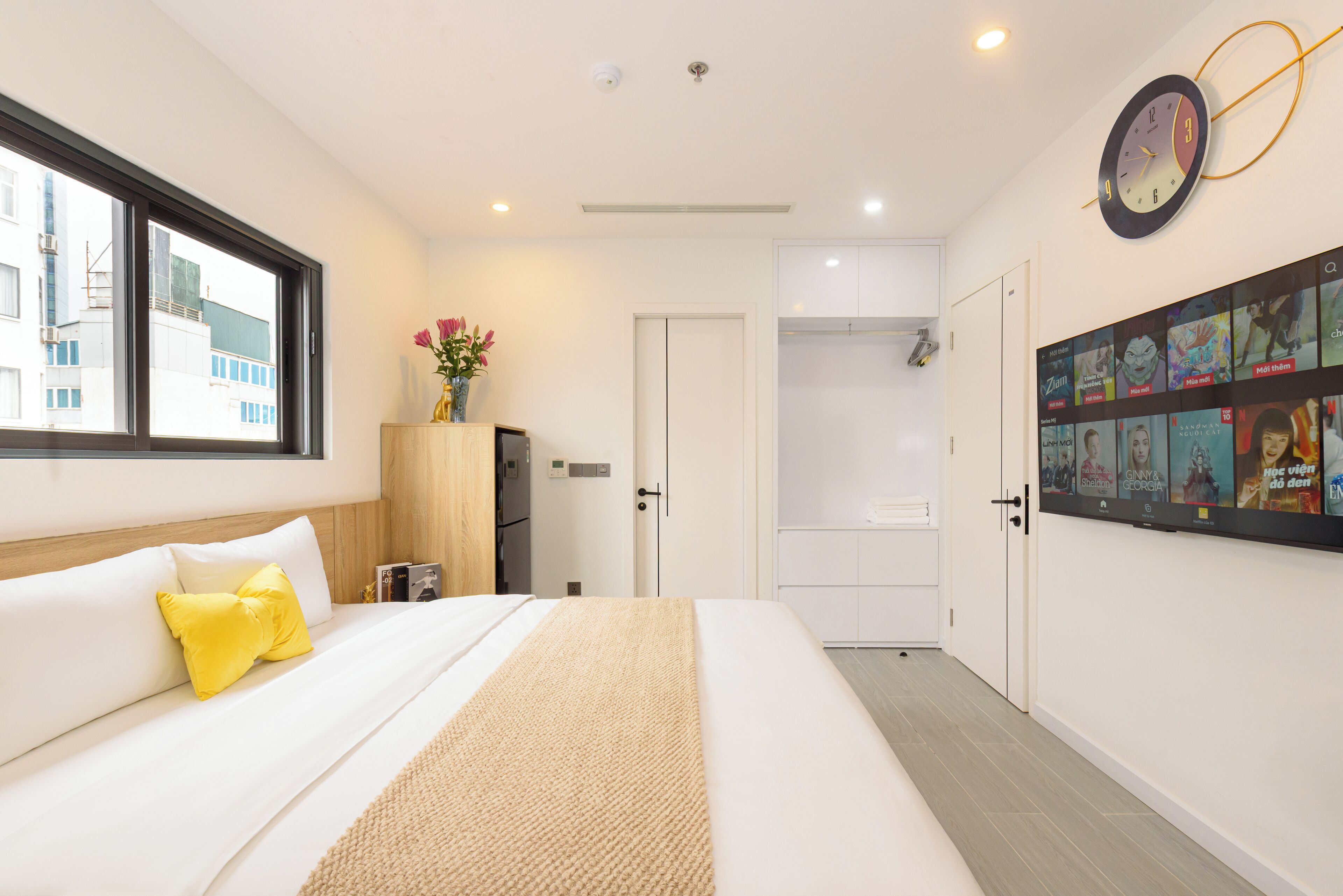 Una camera d'albergo moderna con un letto, una finestra, una sveglia e una parete con poster.