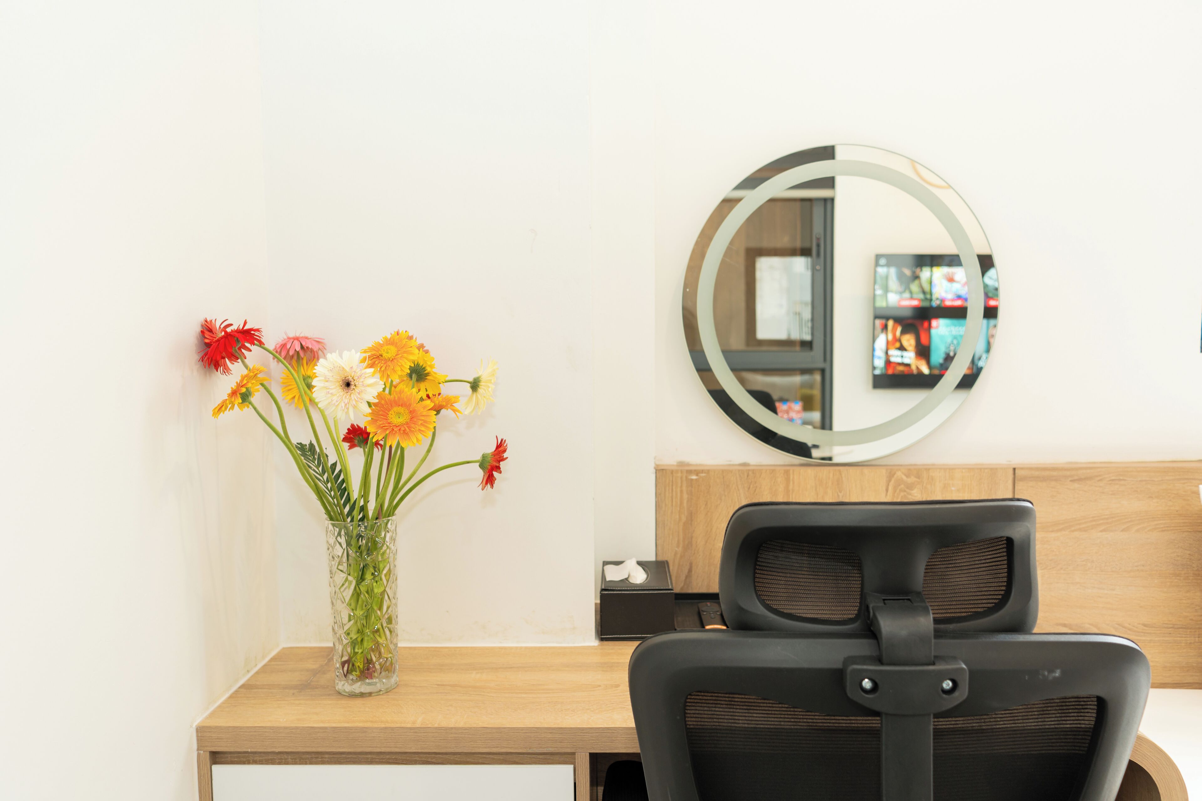 Un bureau orné d’un vase de fleurs, un miroir rond et une chaise de bureau noire.
