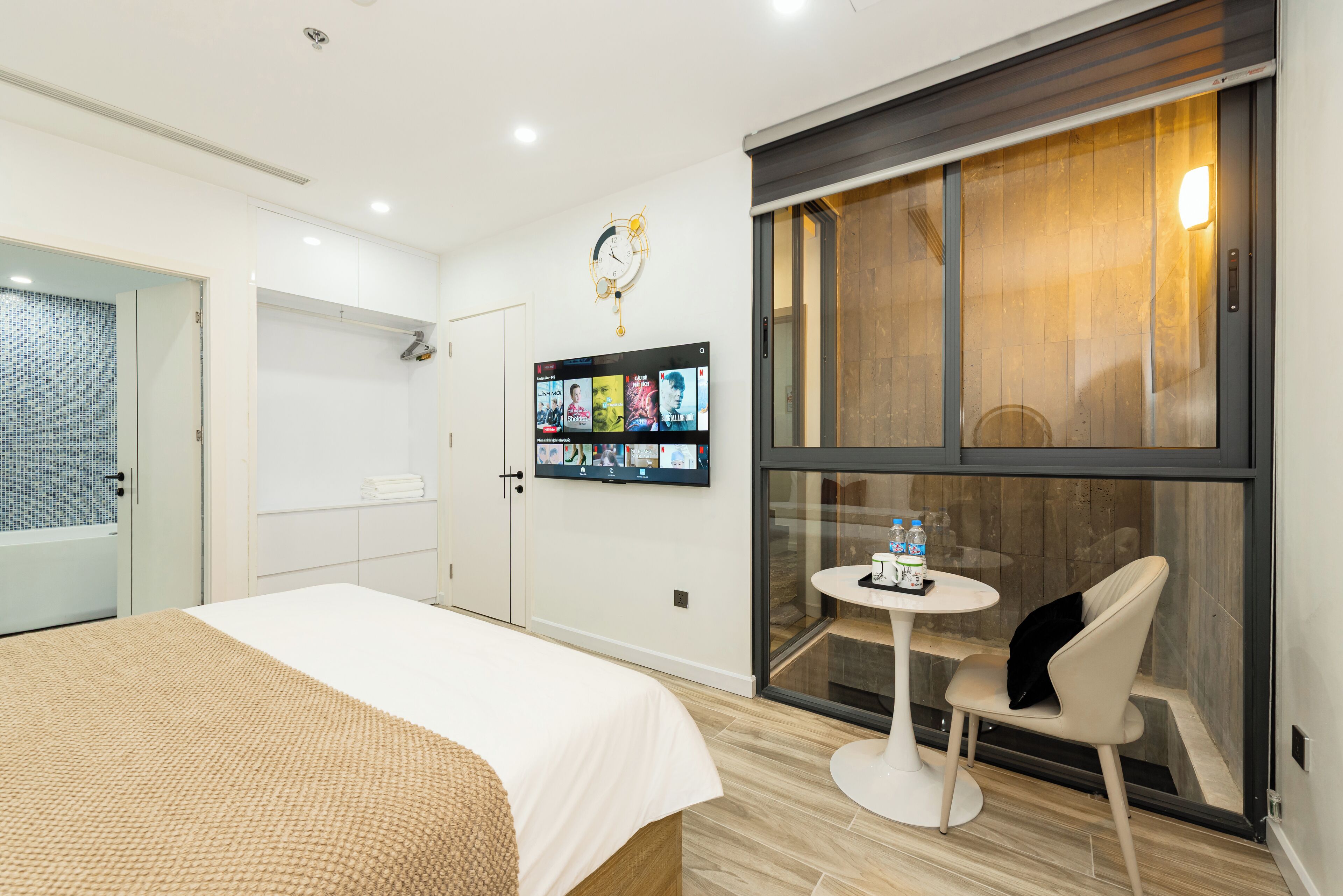 Habitación de hotel con cama, una mesita con silla, televisor montado en la pared y ventana con vista al exterior.