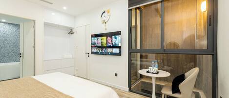 Habitación de hotel con cama, una mesita con silla, televisor montado en la pared y ventana con vista al exterior.