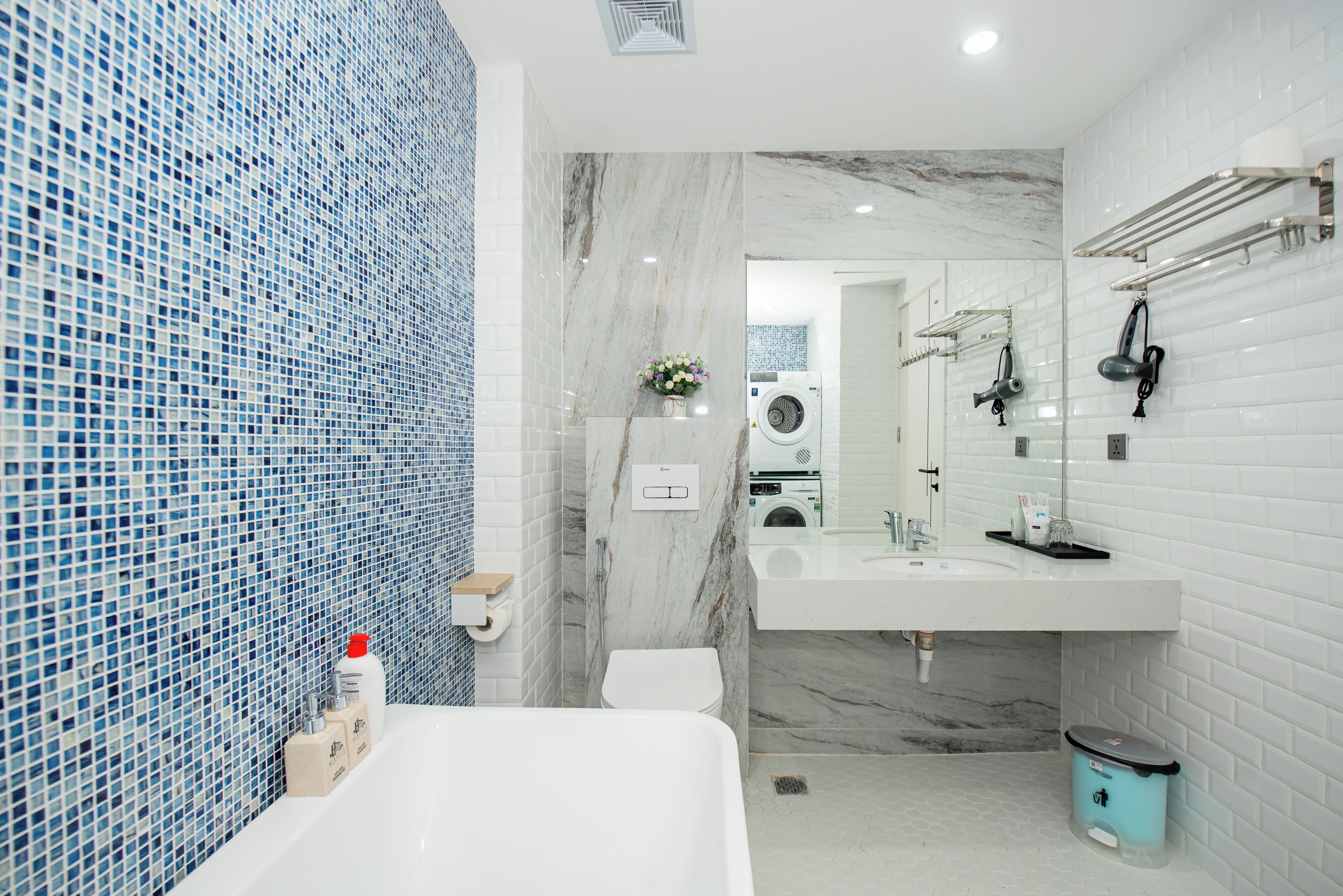 Ein modernes Badezimmer mit einem Marmorwaschbecken, einer weißen Toilette, einer blauen Mülltonne und einer Wand aus blauen Mosaikfliesen.