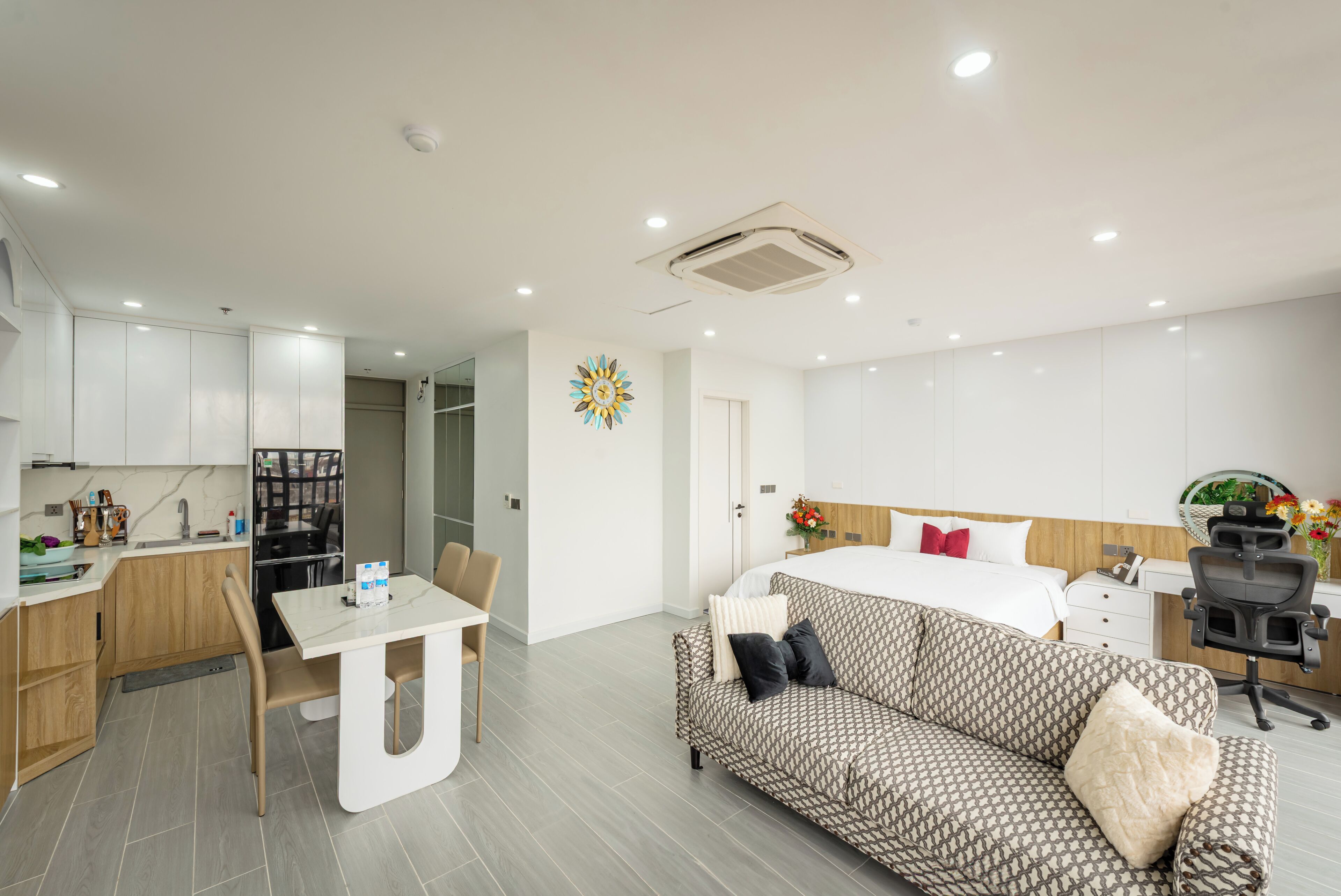 A modern hotel room with a bed, a sofa, a dining area, and a kitchenette.