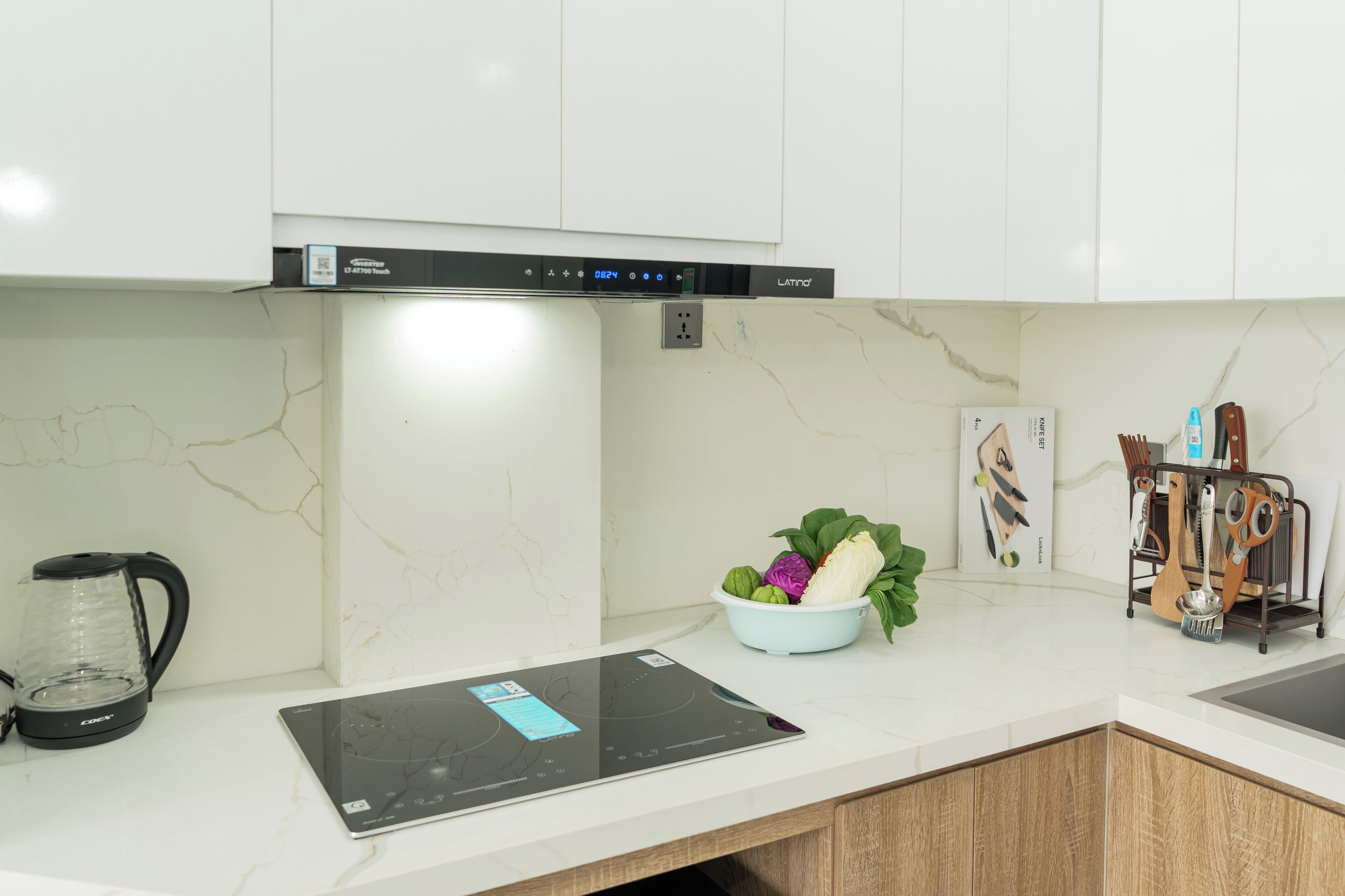A kitchen with a built-in induction cooktop, a coffee maker, a bowl of fruit, and a utensil holder.