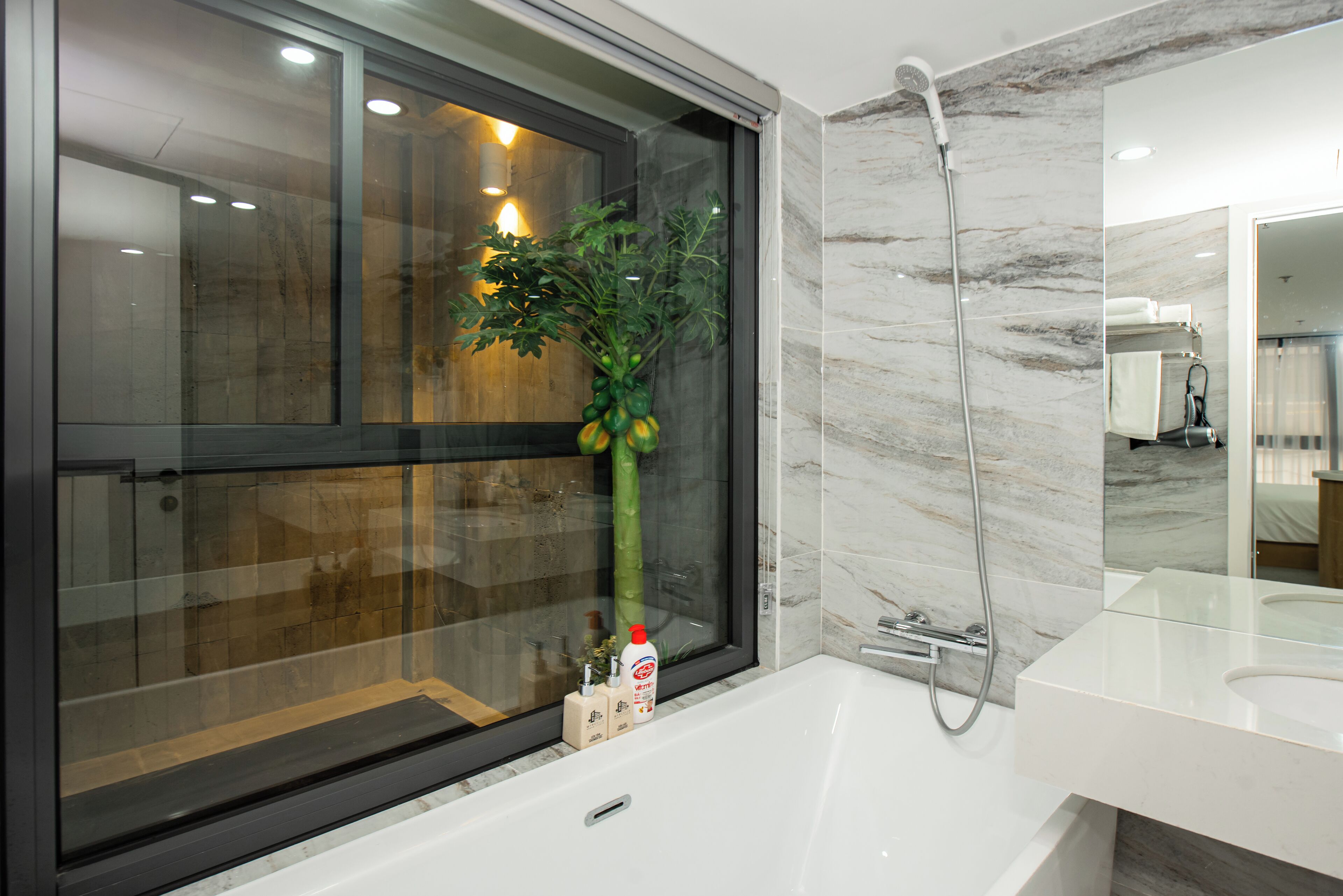 Een moderne badkamer met een glazen douchecabine, een witte badkuip en een marmeren wand.