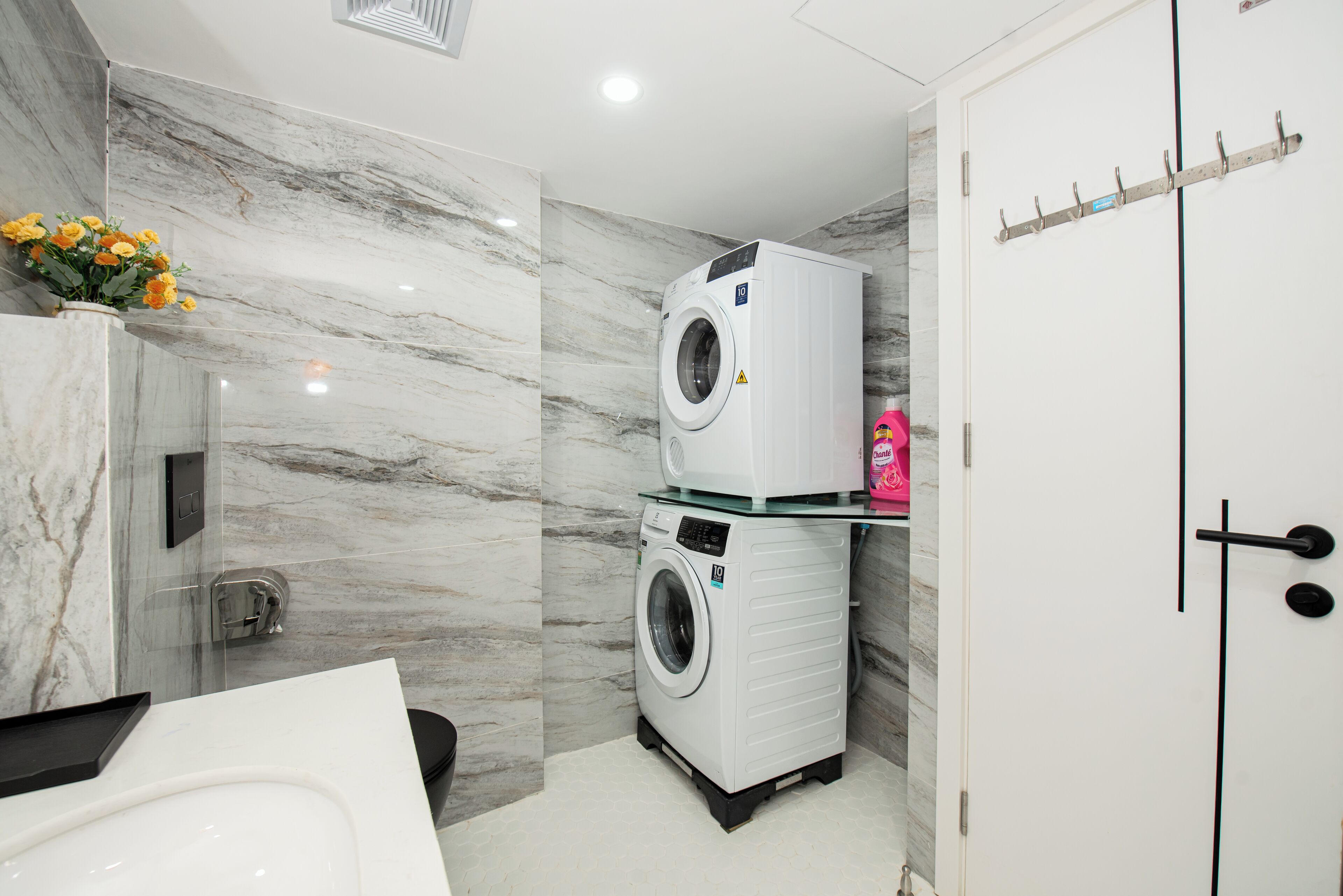 A modern bathroom with a marble wall, a washing machine, a toilet, and a sink.