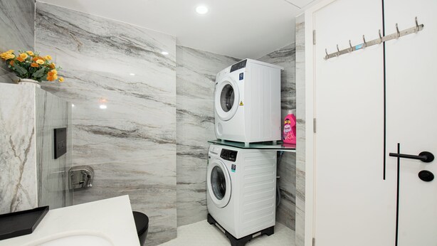 A modern bathroom with a marble wall, a washing machine, a toilet, and a sink. - Myrcella Apartment  (Hanoi)